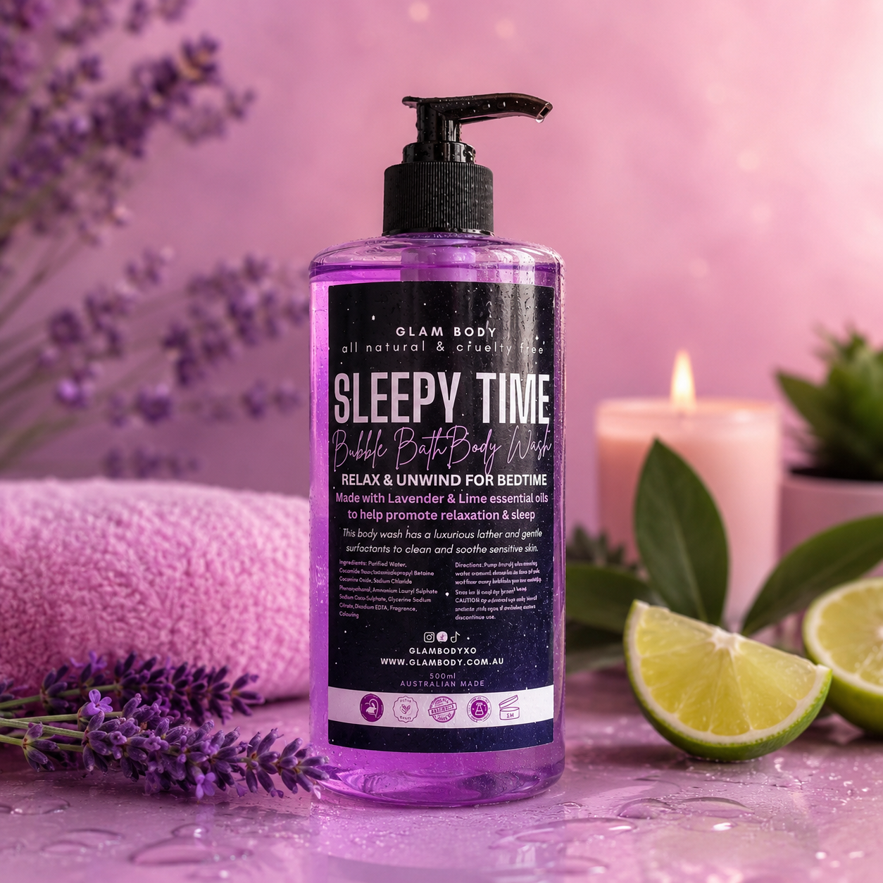 A bottle of Glam Body 'Sleepy Time' bubble bath body wash stands on a glossy pink surface with lavender sprigs, lime wedges, a pink towel, and a lit candle in the background.