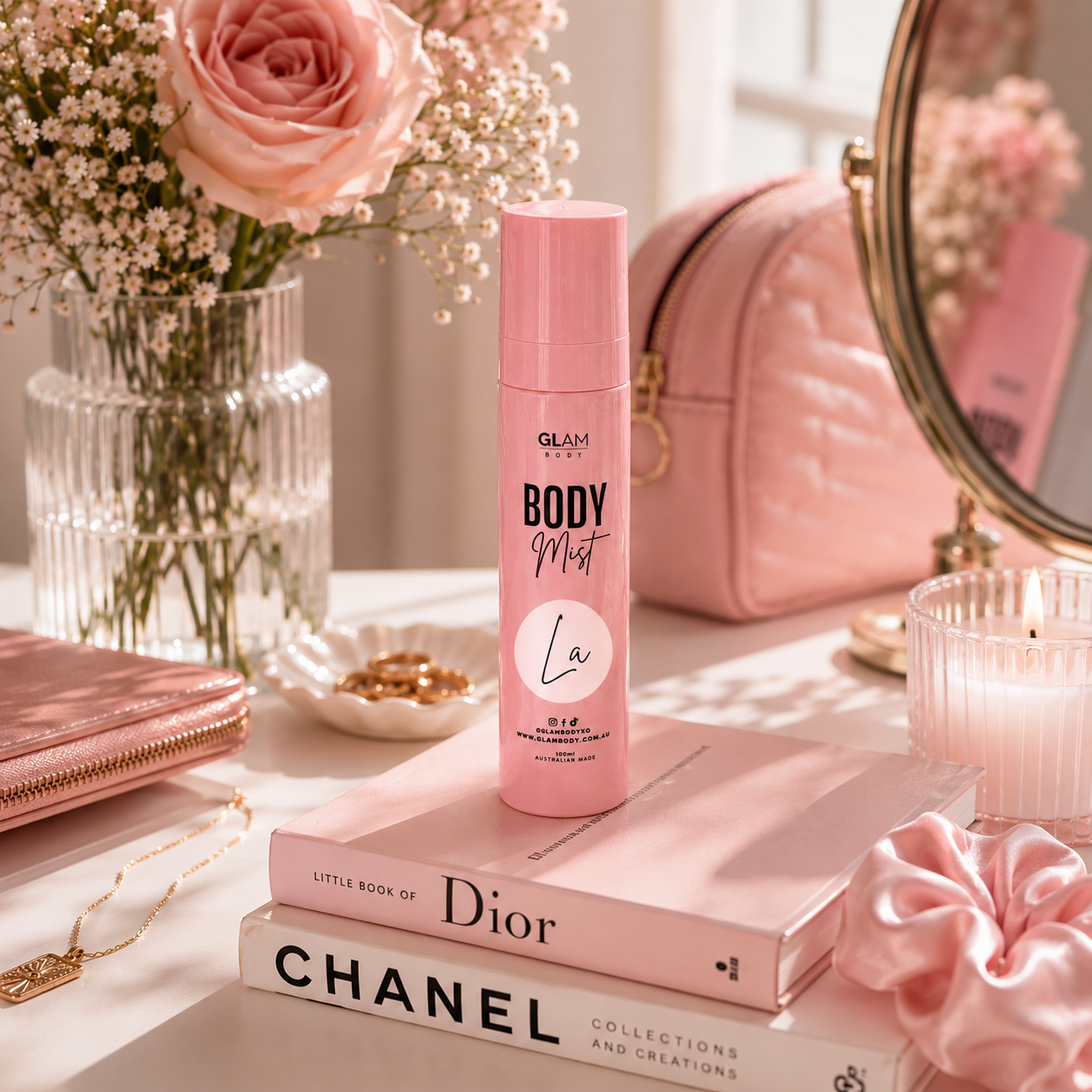 Pink 'Body Mist' bottle on books with flowers and a mirror in the background