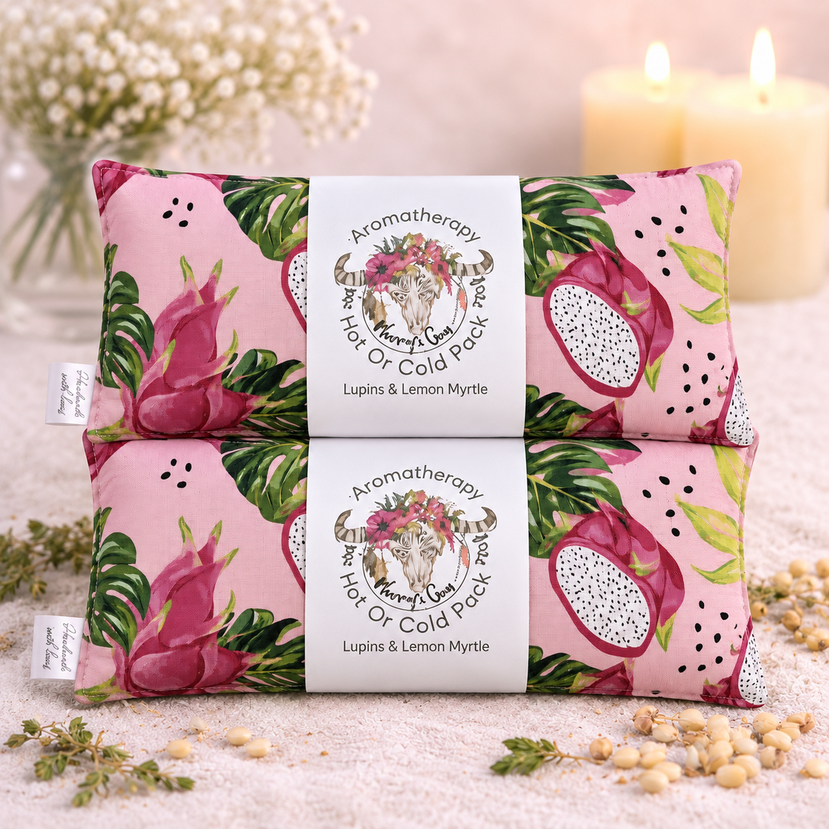 Two pink aromatherapy hot or cold packs stacked vertically, decorated with a tropical dragon fruit and linden leaf pattern, with a white paper band in the center reading 'Aromatherapy Hot or Cold Pack' and 'Lupins & Lemon Myrtle'.
