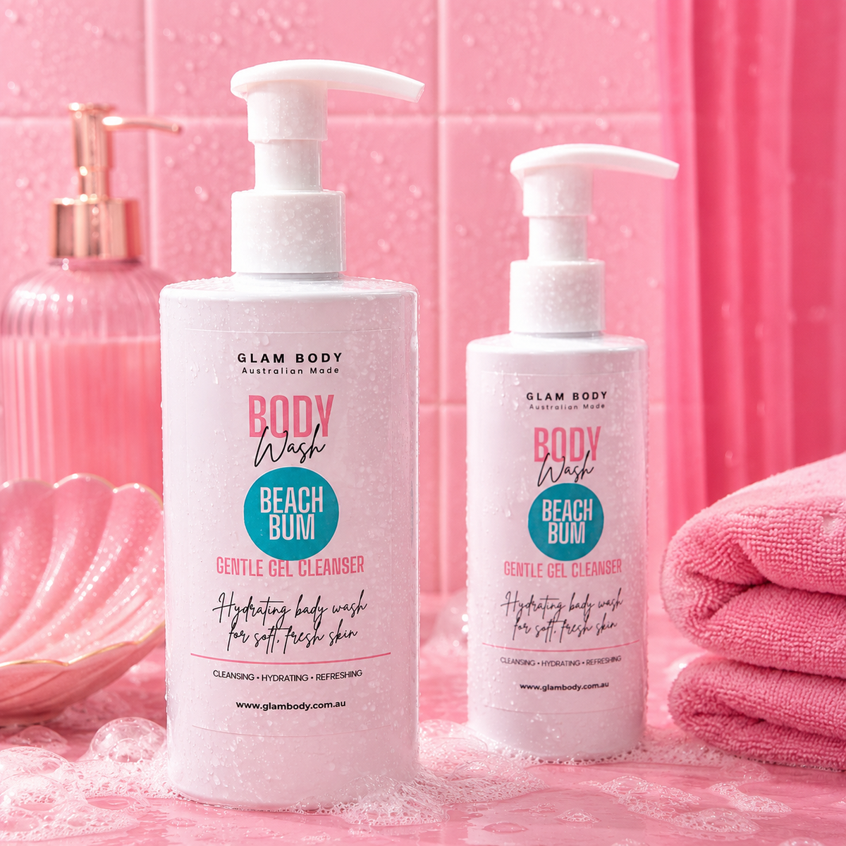 Two bottles of Glam Body Beach Bum Gentle Gel Cleanser with white pump dispensers, set against a pink tiled background with a pink towel and soap dish.