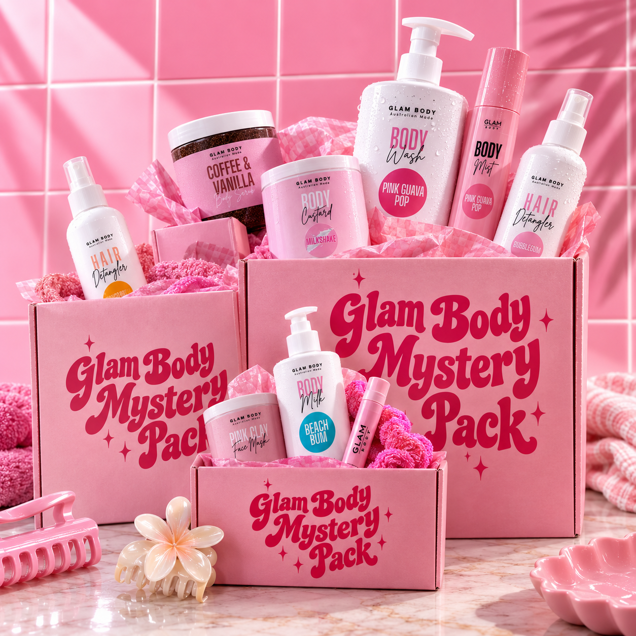 Three pink Glam Body Mystery Pack boxes filled with bath and body products, including body wash, shampoo, hair oil, and lotions, arranged on a pink-tiled surface with pink props.