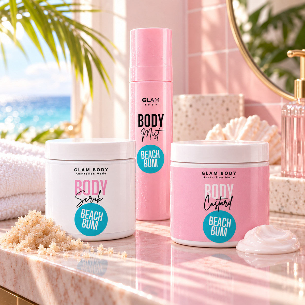 Three Glam Body beach bum skincare products arranged on a pink marble countertop with a beach and palm leaves in the background: a white tub of Body Scrub, a pink bottle of Body Moist, and a pink tub of Body Custard, each labeled Beach Bum.