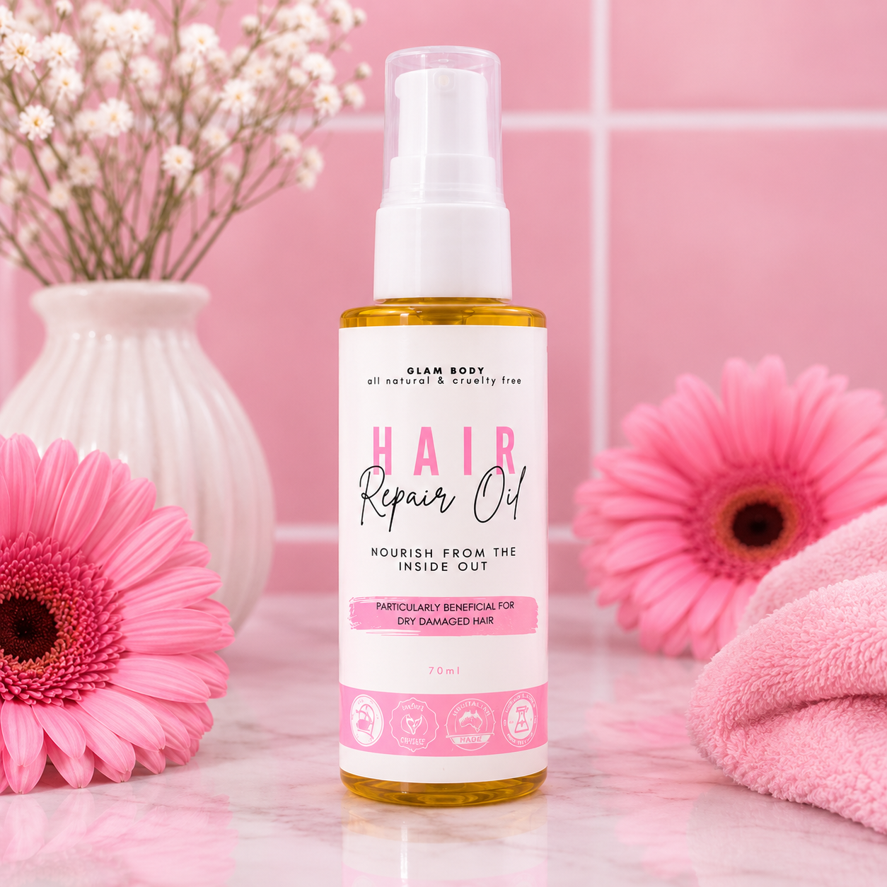 A bottle of Giam Body Hair Repair Oil stands on a pink marble surface with pink flowers and a pink towel around it. The product is a clear spray bottle filled with golden-yellow liquid, featuring a white label with pink and black text.