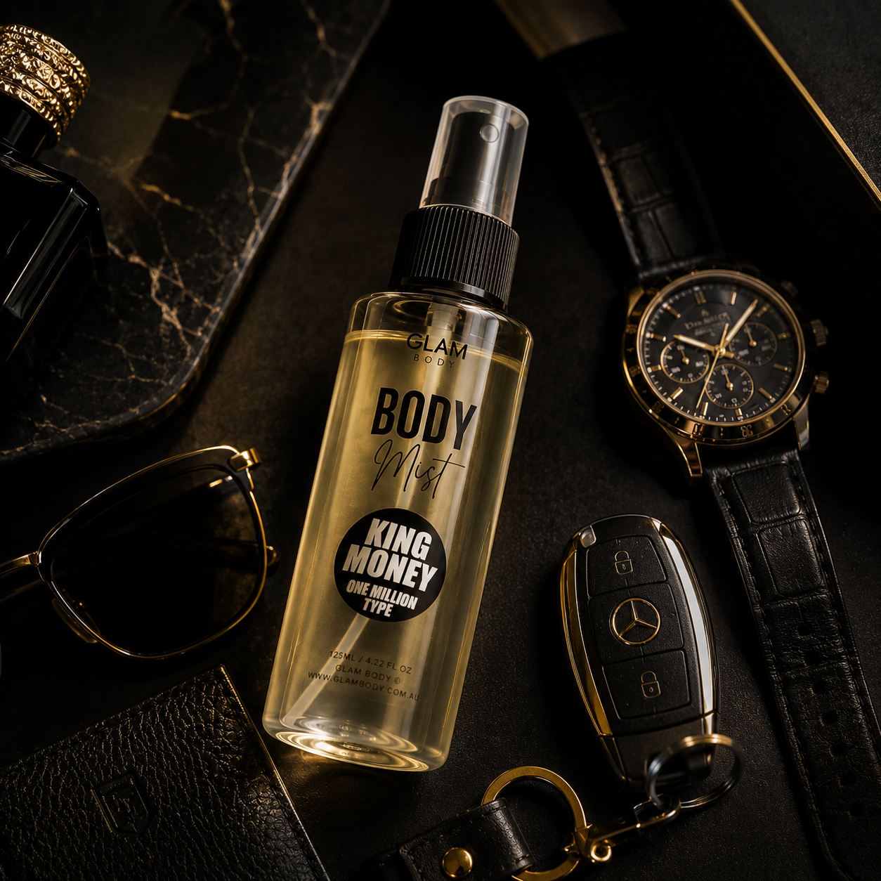 Body mist bottle labeled 'King Money' with a watch, sunglasses, and car keys on a dark surface.