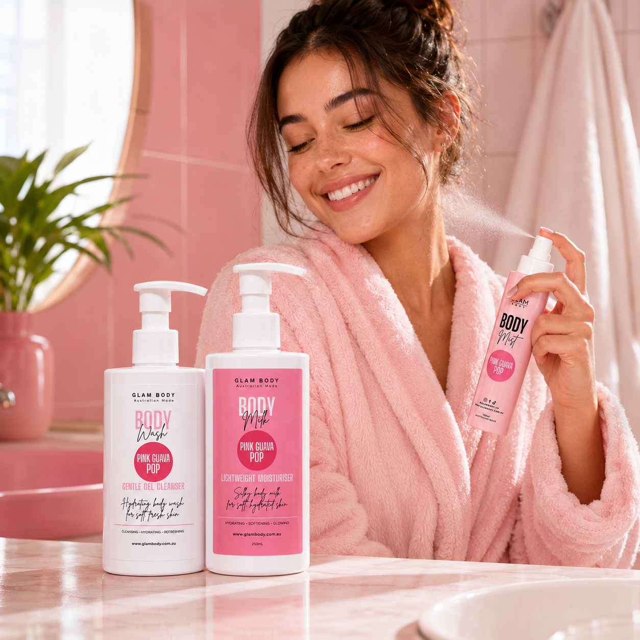 A woman in a pink bathrobe smiles while spraying a body wash from Slim Body Body Reviver. Two Slim Body body wash bottles are displayed on a marble bathroom counter in front of a pink tiled wall.
