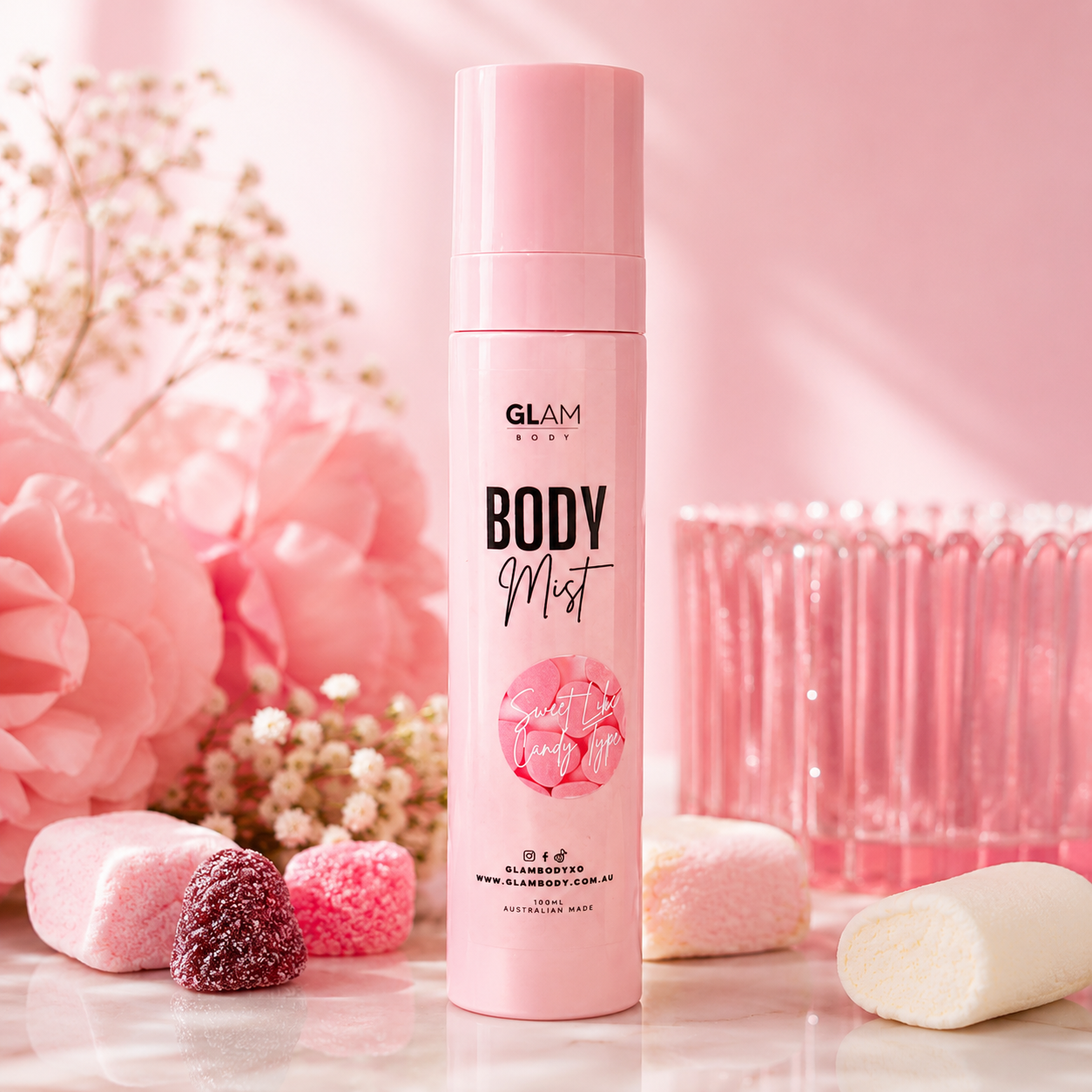 Pink 'GLAM' body mist bottle with decorative flowers and candies on a pink background