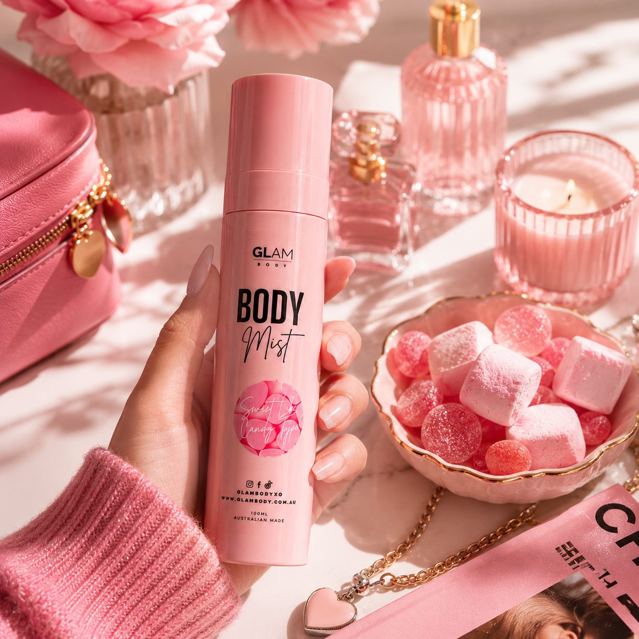 Hand holding a pink 'GLAM' body mist with a decorative background