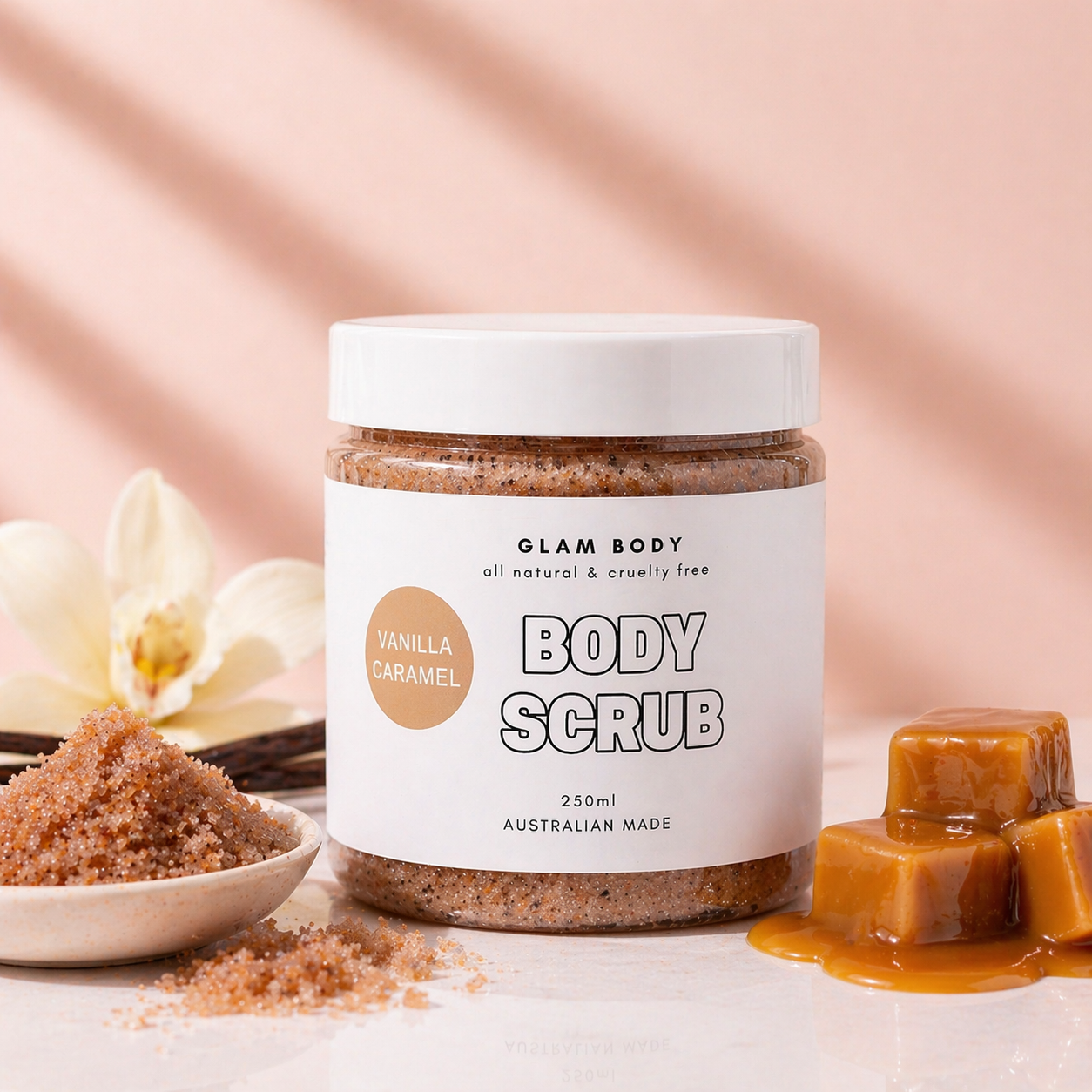 Jar of Glam Body Vanilla Caramel body scrub with caramel candies and orchids on a peach background