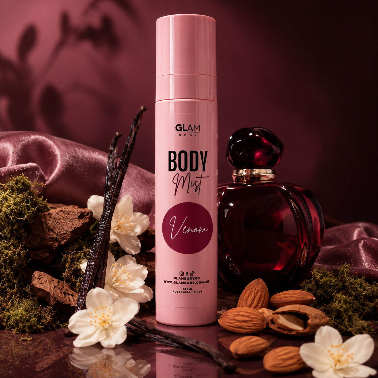Pink 'BODY MIST' spray bottle with vanilla beans, flowers, and almonds on a dark background
